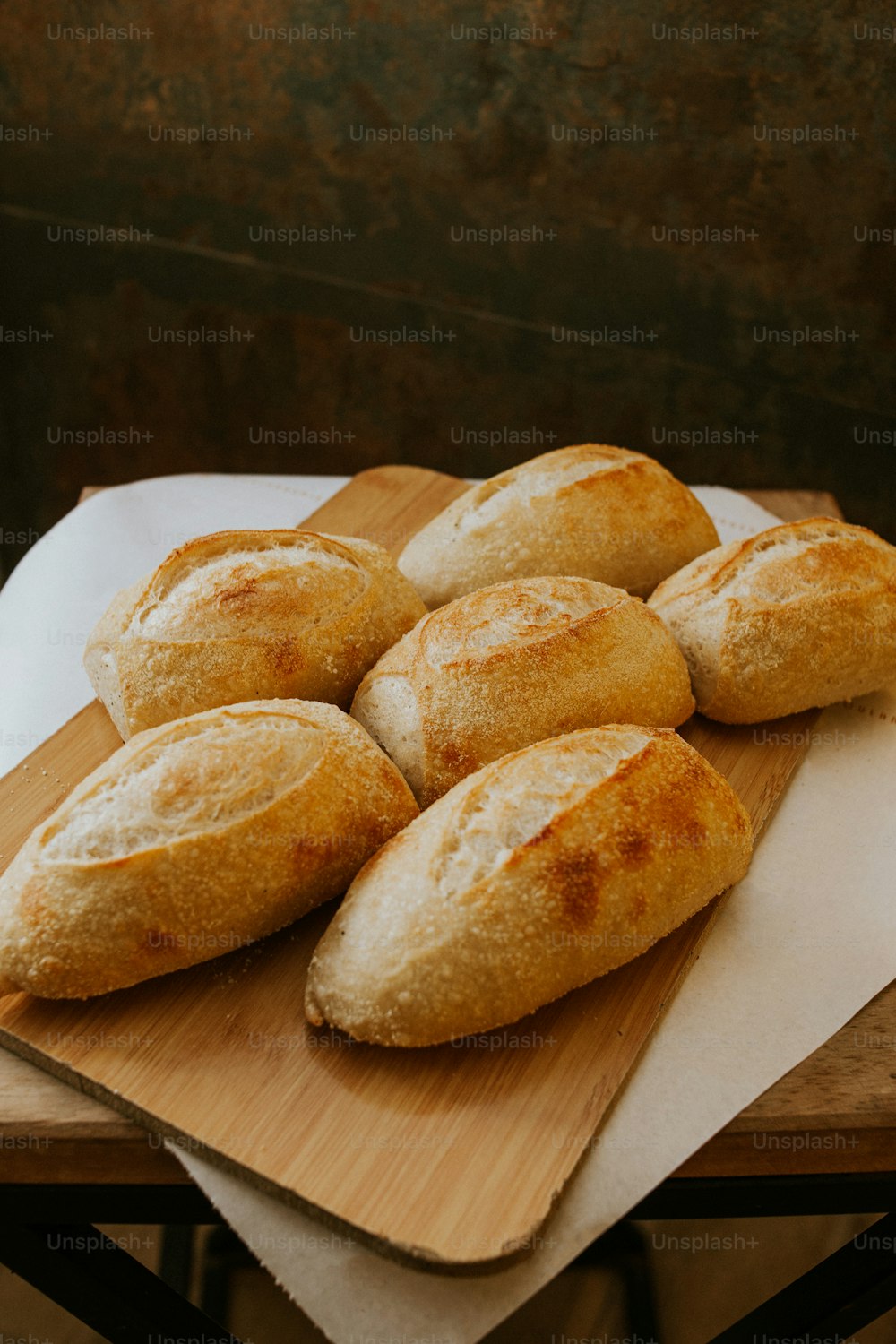 a wooden cutting board topped with rolls on top of a table