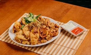 a white plate topped with fried food next to a bowl of sauce