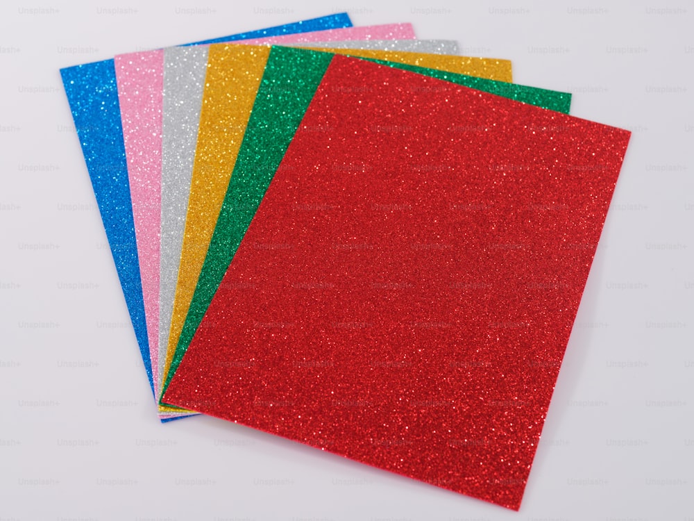 una pila di carta glitterata di diversi colori su una superficie bianca