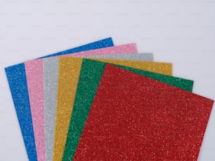 a pile of different colored glitter paper on a white surface
