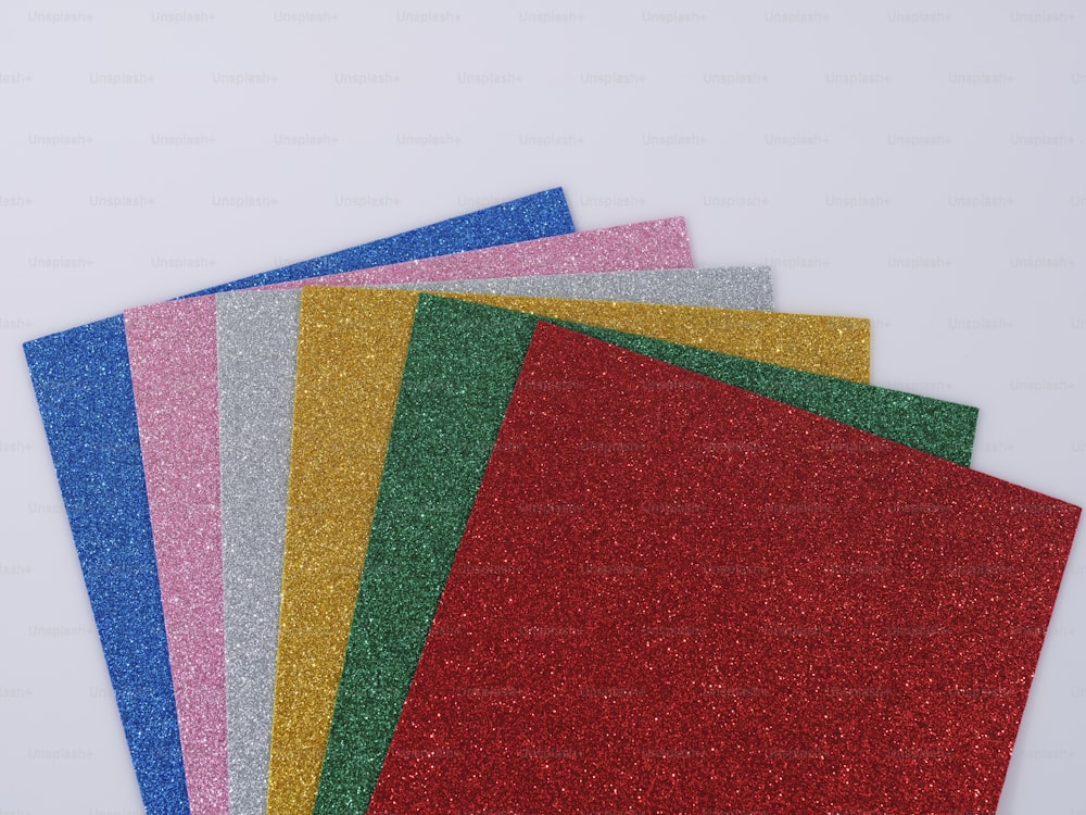 a pile of different colored glitter paper on a white surface