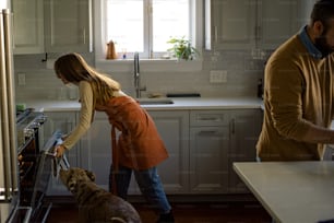 a man and a woman in a kitchen with a dog