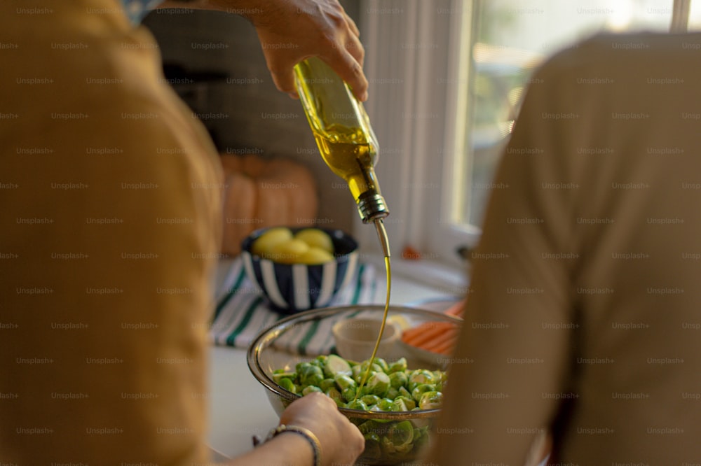 a person pouring olive oil into a bowl of vegetables