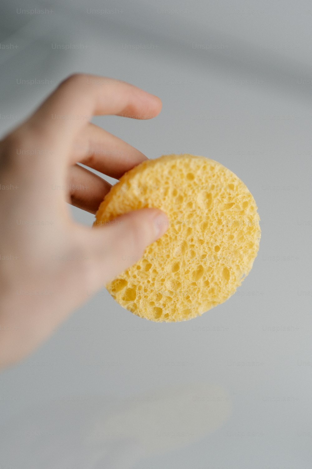 a hand holding a sponge over a white surface