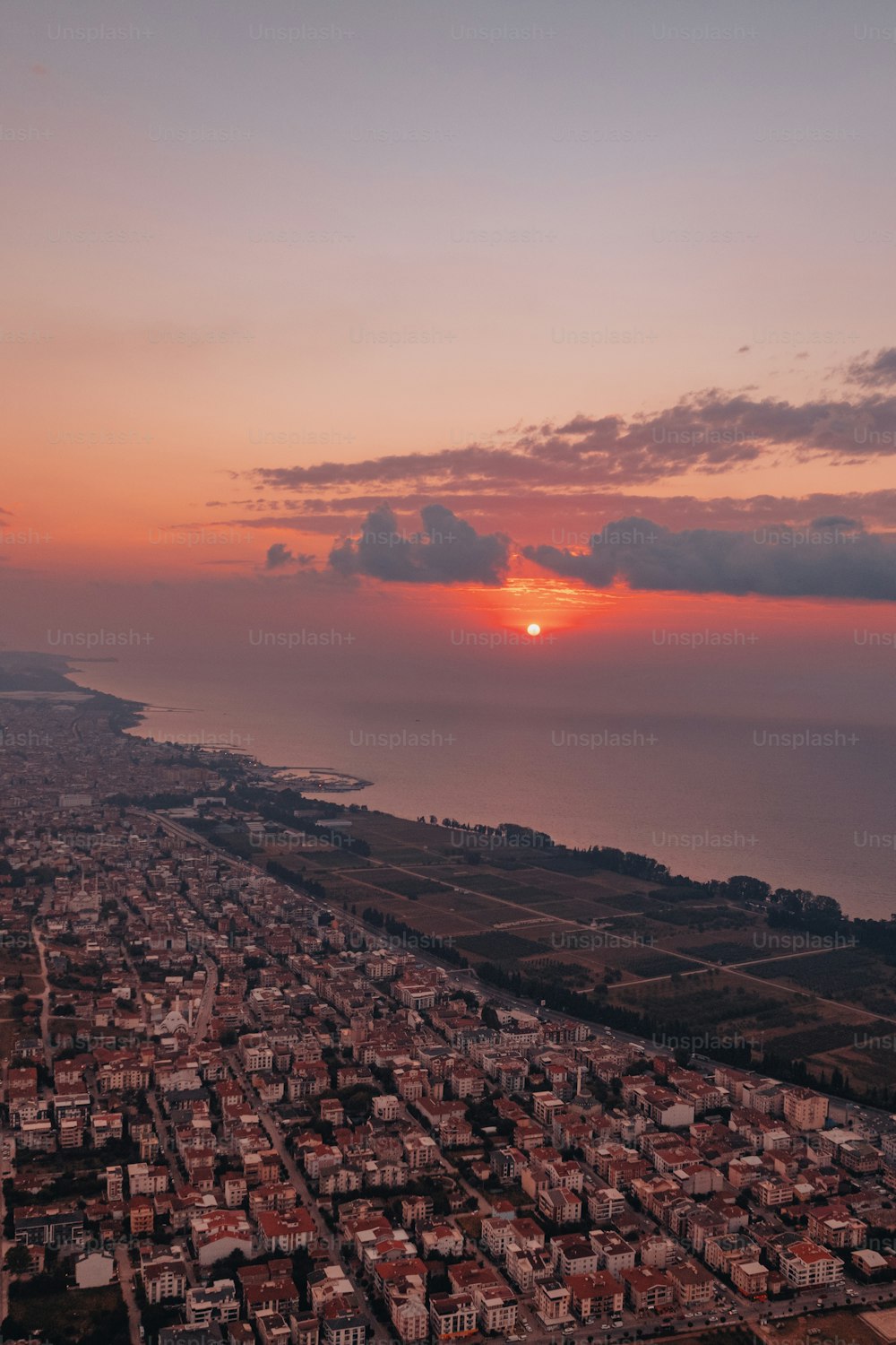 the sun is setting over a city by the ocean