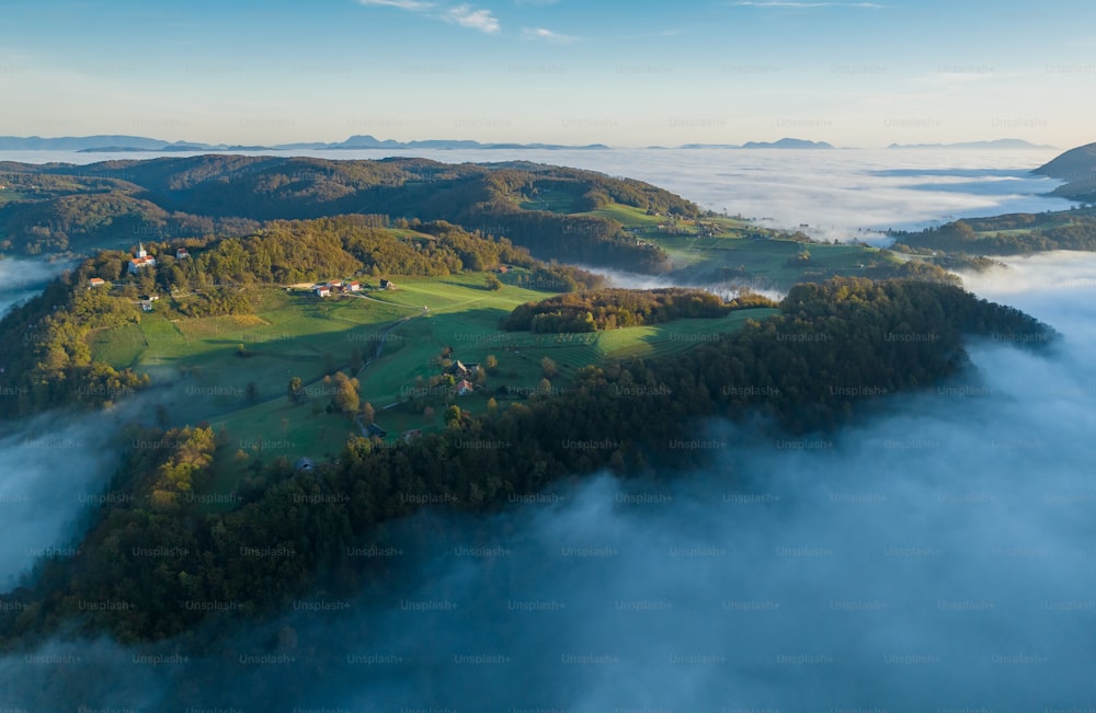 an aerial view of a green valley surrounded by fog