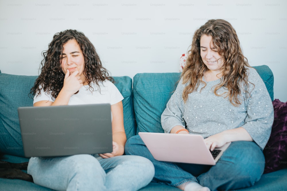 two women sitting on a couch with laptops