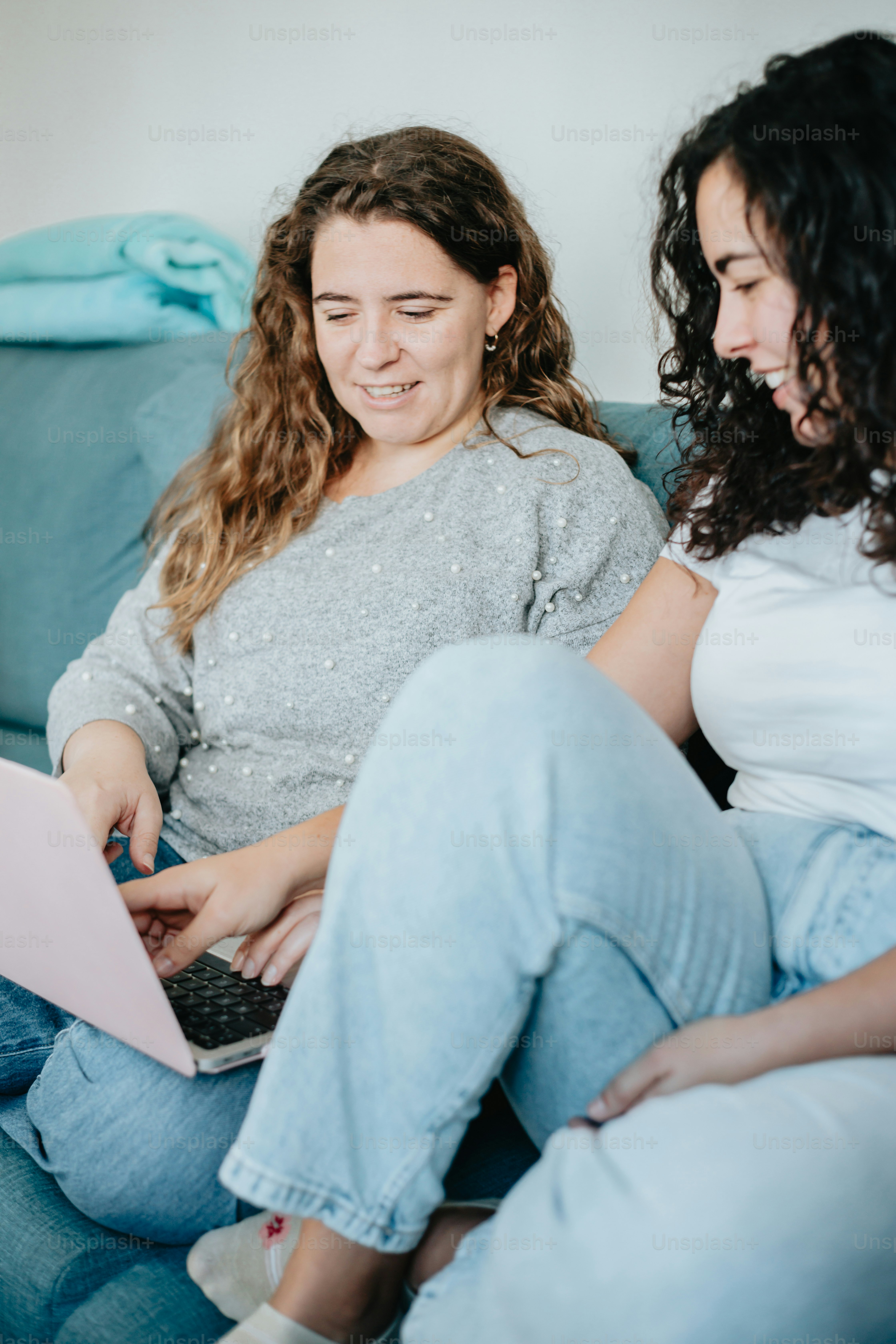 two women sitting on a couch looking at a laptop