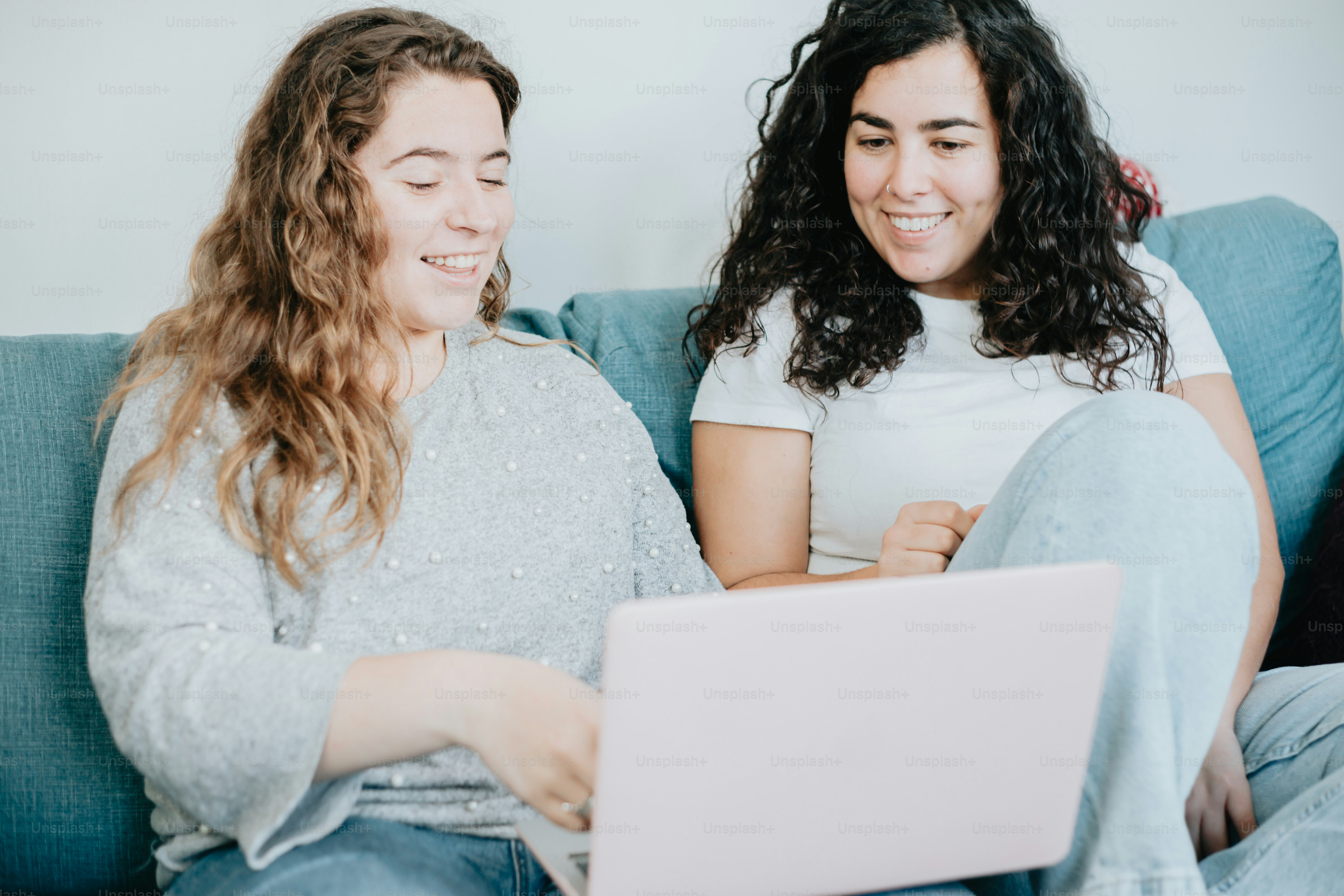 two women sitting on a couch looking at a laptop
