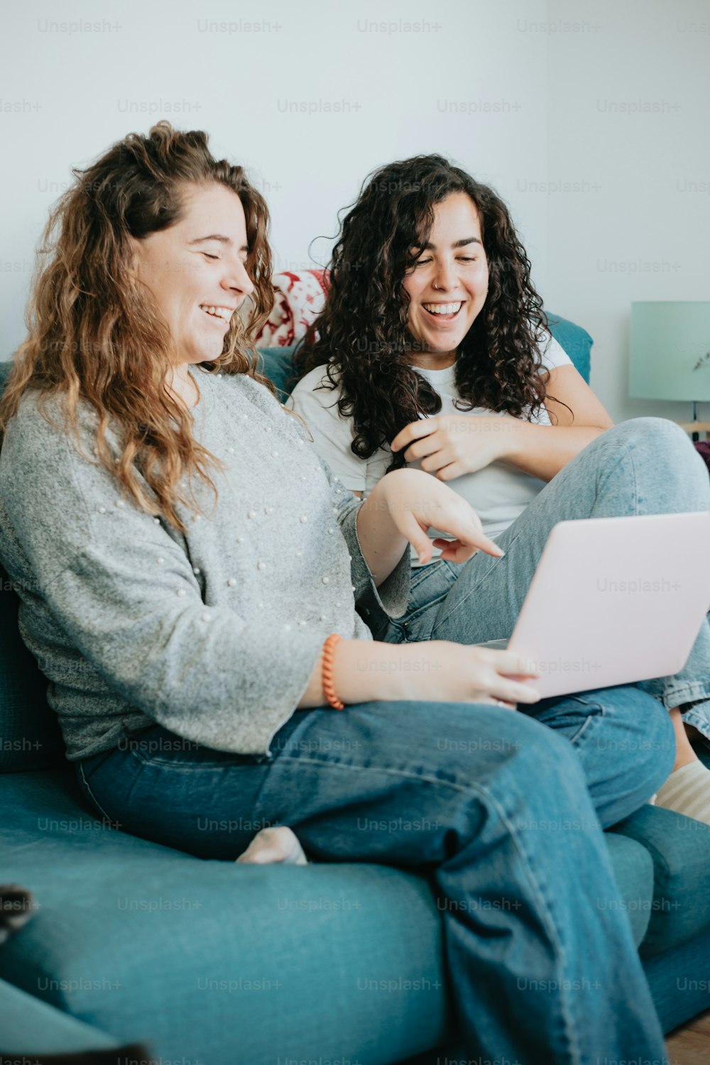 two women sitting on a couch with a laptop