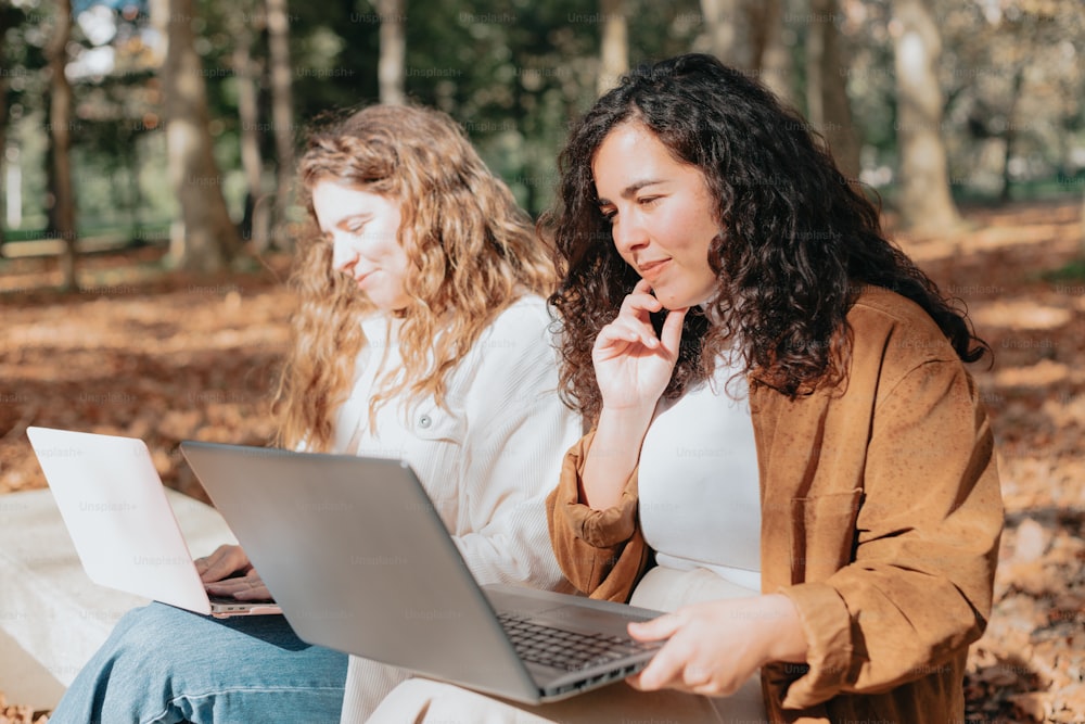 a couple of women sitting on the ground with a laptop