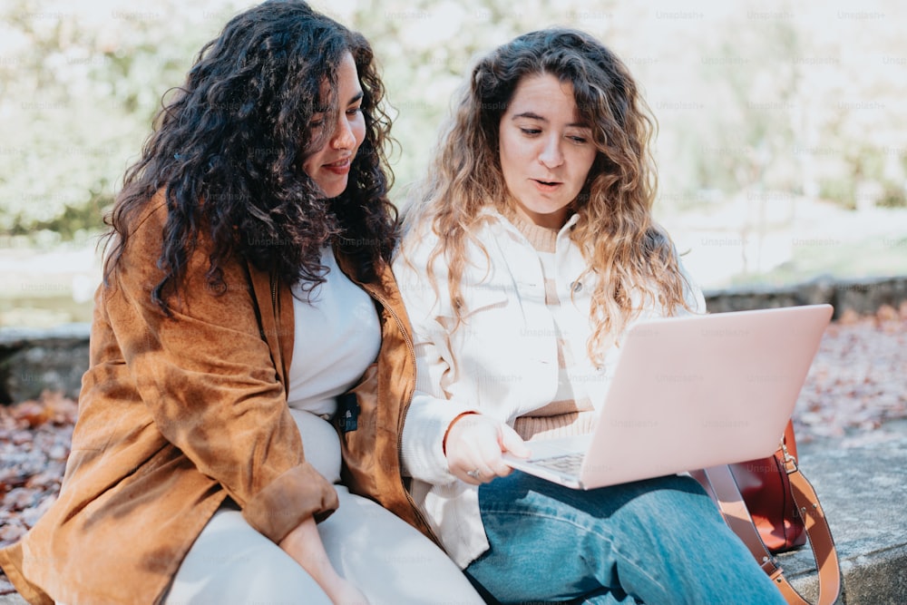 two women sitting on a bench looking at a laptop