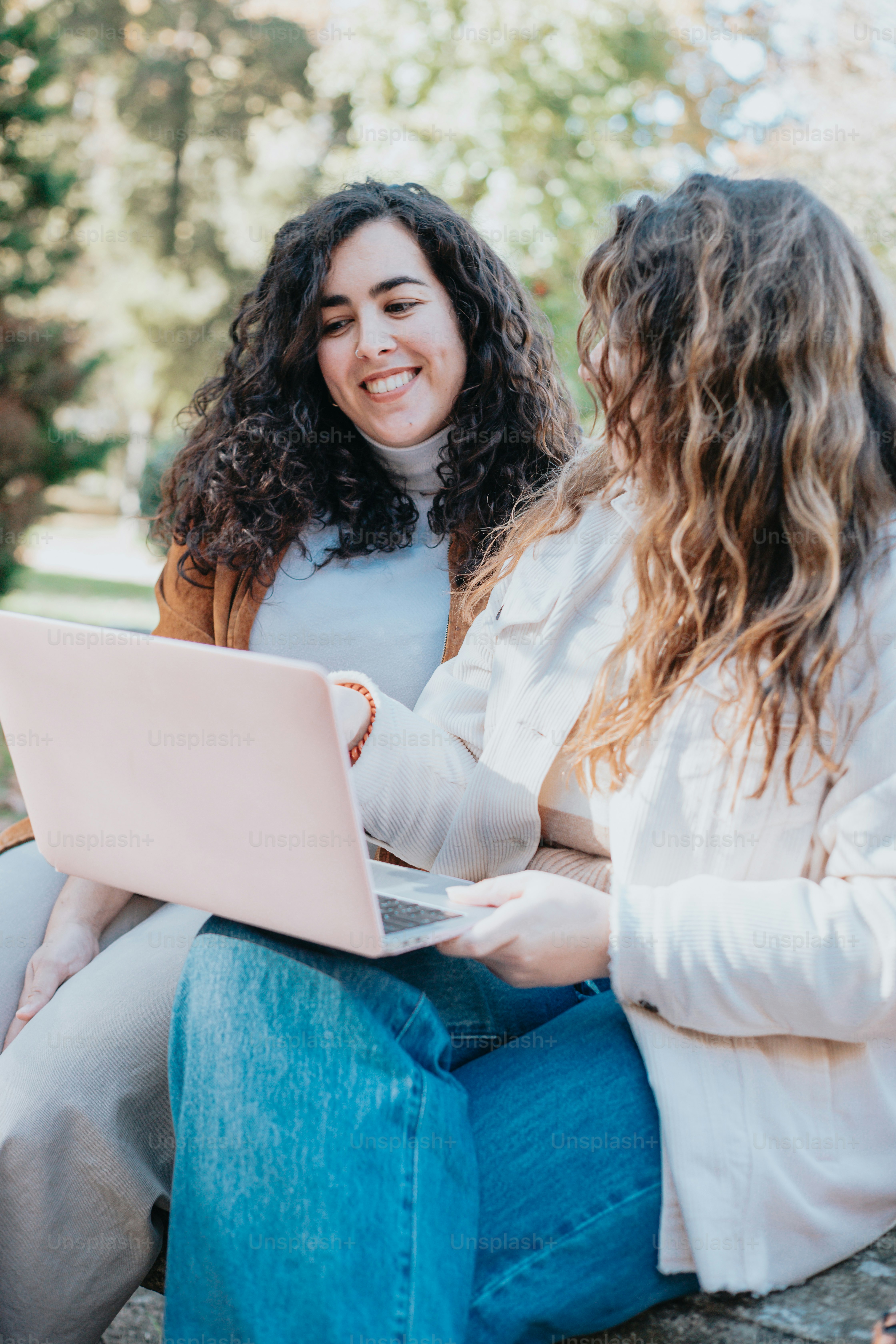 two women sitting on a rock looking at a laptop