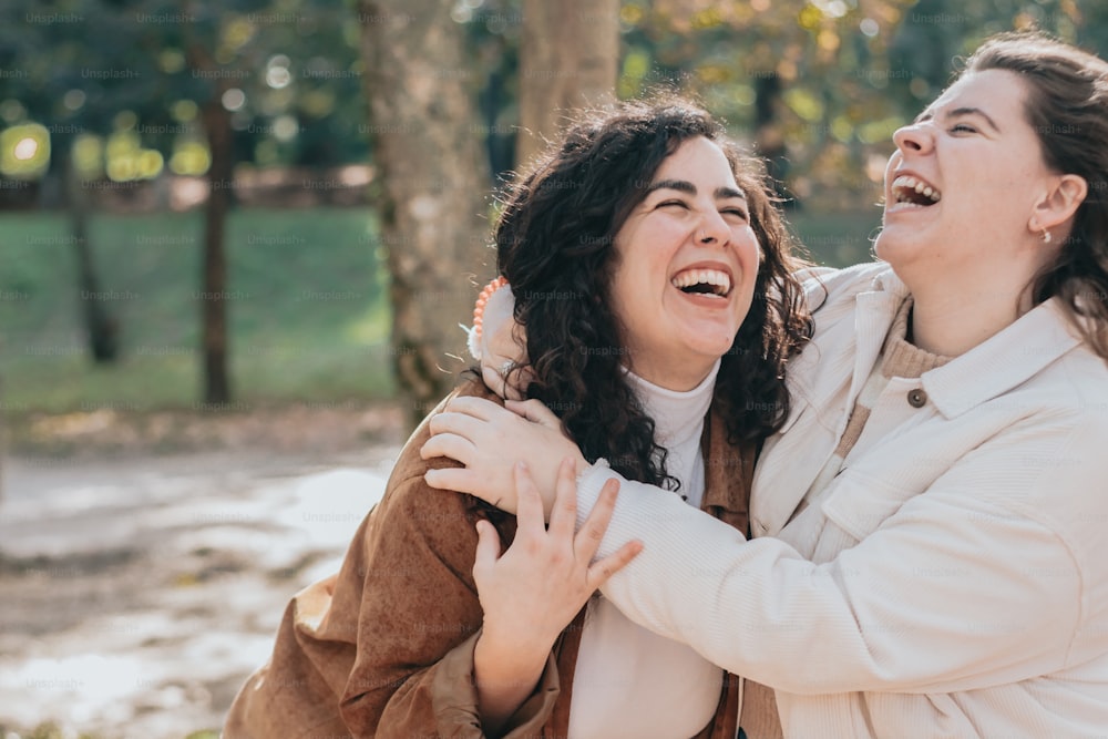 two women laughing and hugging each other in a park