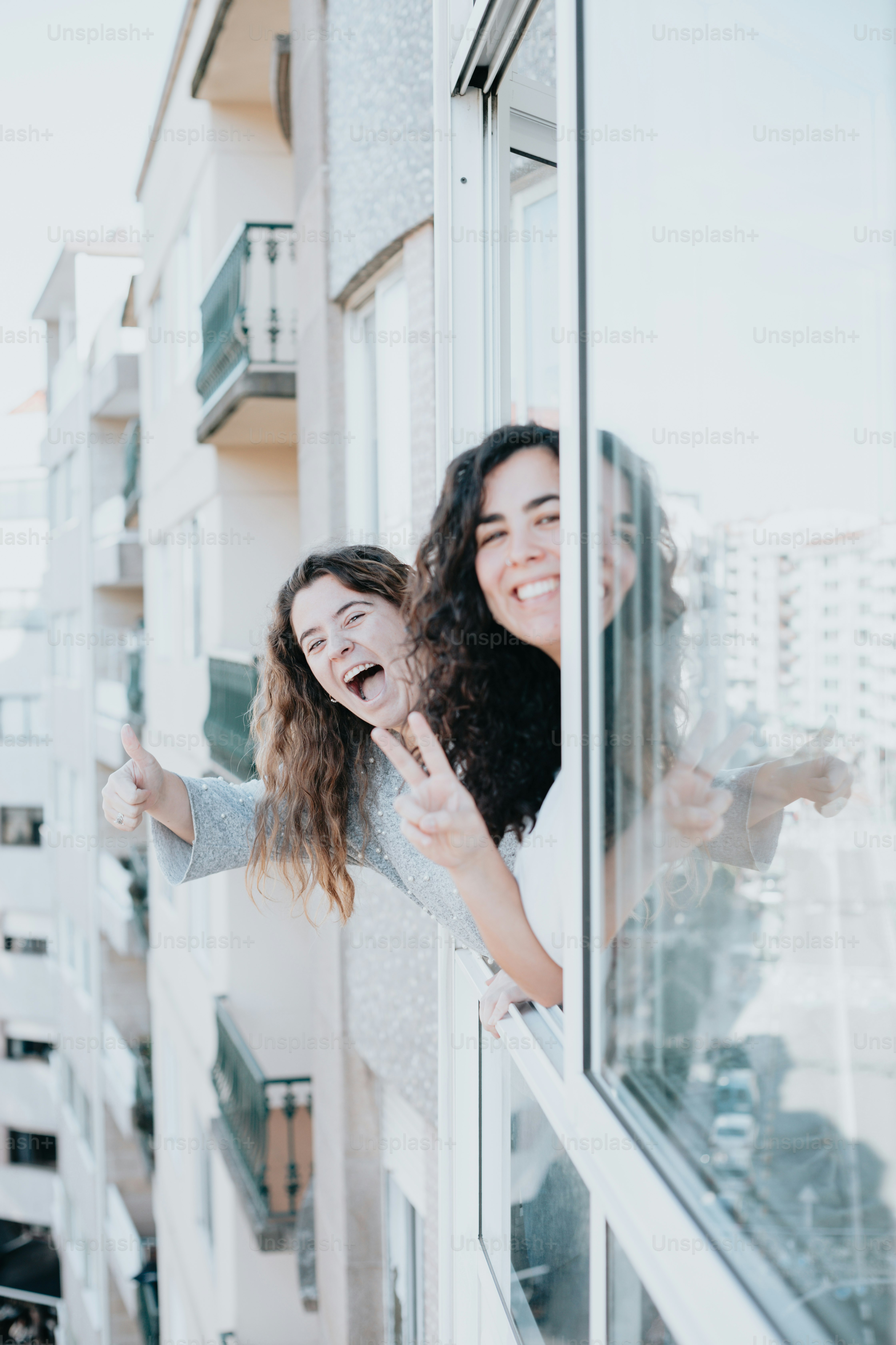 duas mulheres em pé no peitoril de uma janela e sorrindo