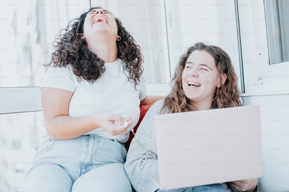 two women laughing while looking at a laptop