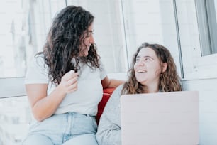 two women sitting on a couch looking at a laptop