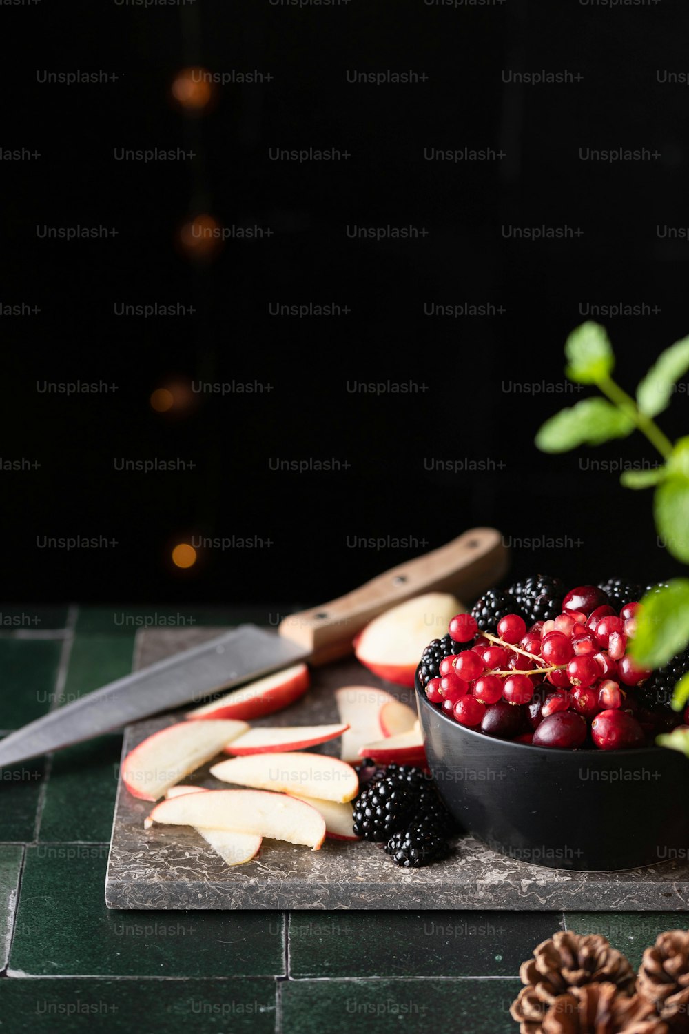 a bowl of berries, apples, and a knife on a cutting board
