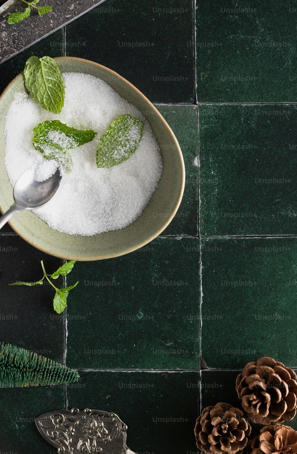 a bowl filled with sugar and mint on top of a green tile floor