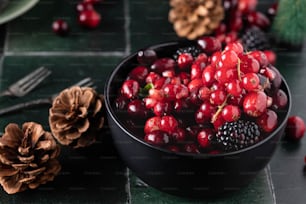 a bowl of berries and pine cones on a table