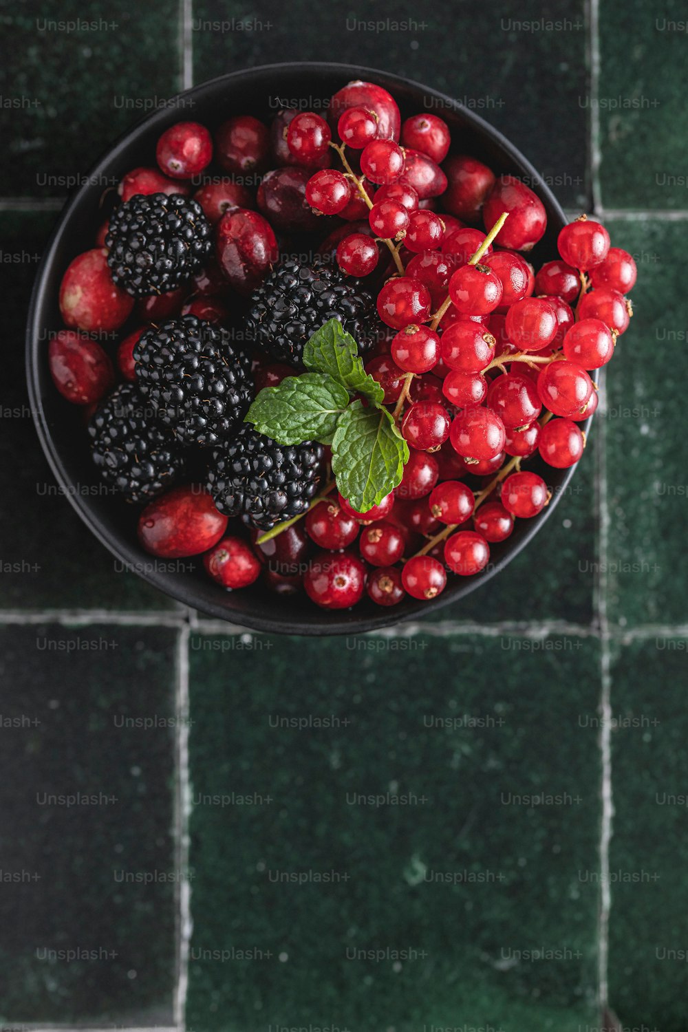 a bowl of berries and blackberries on a green tile floor