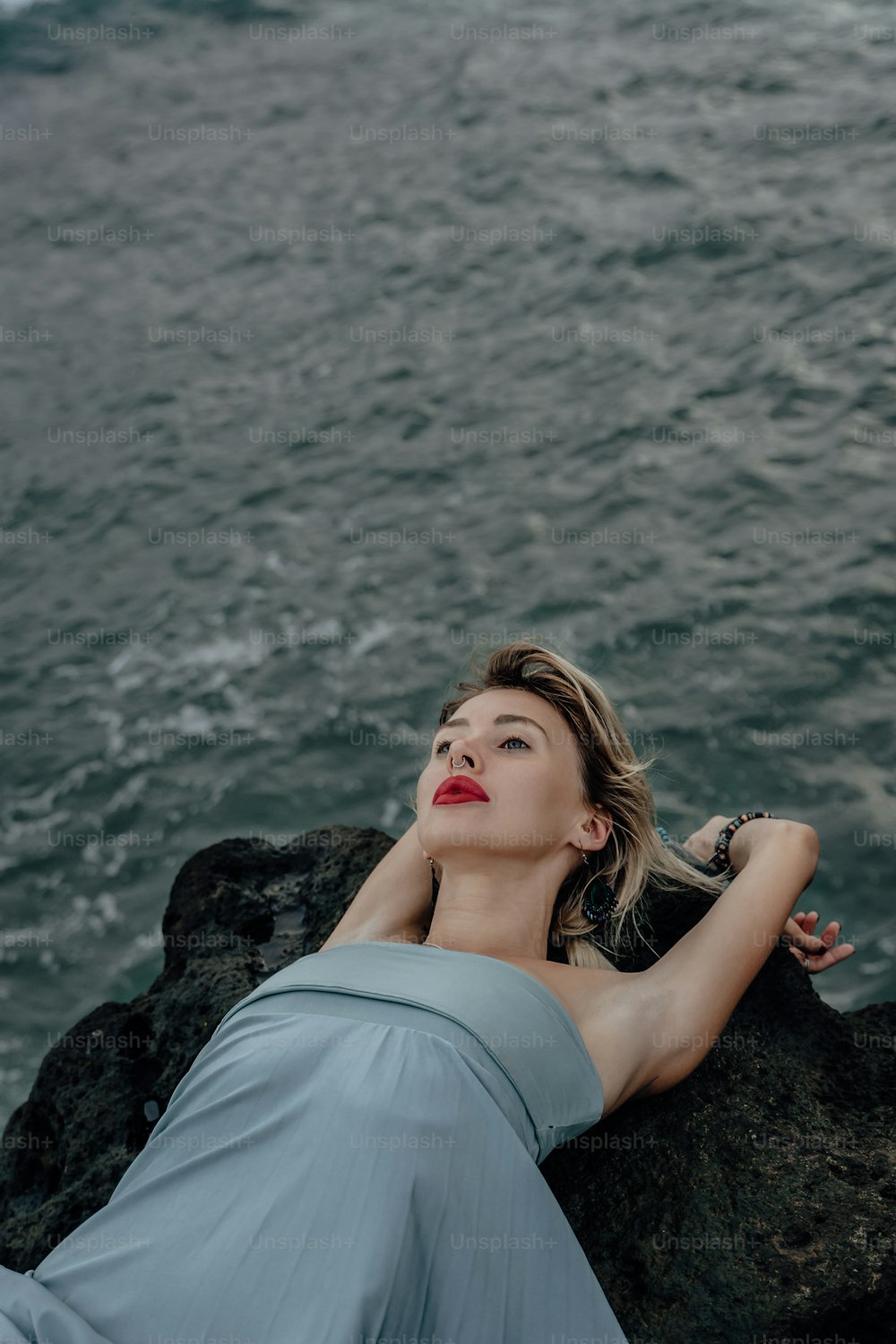 a woman laying on top of a rock next to the ocean