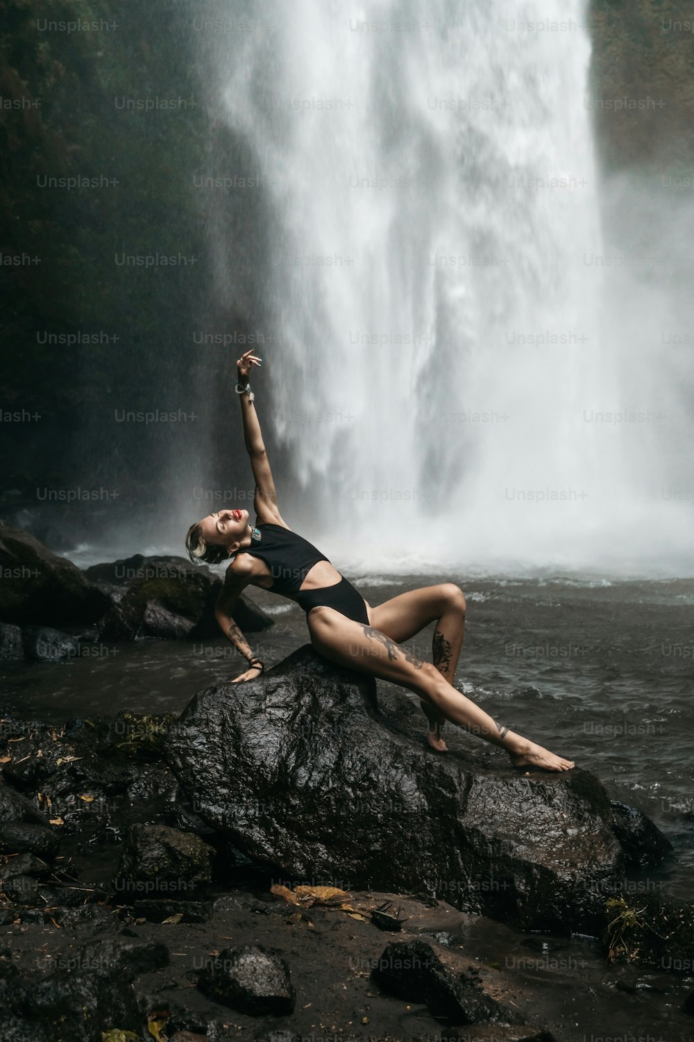 a woman laying on a rock in front of a waterfall