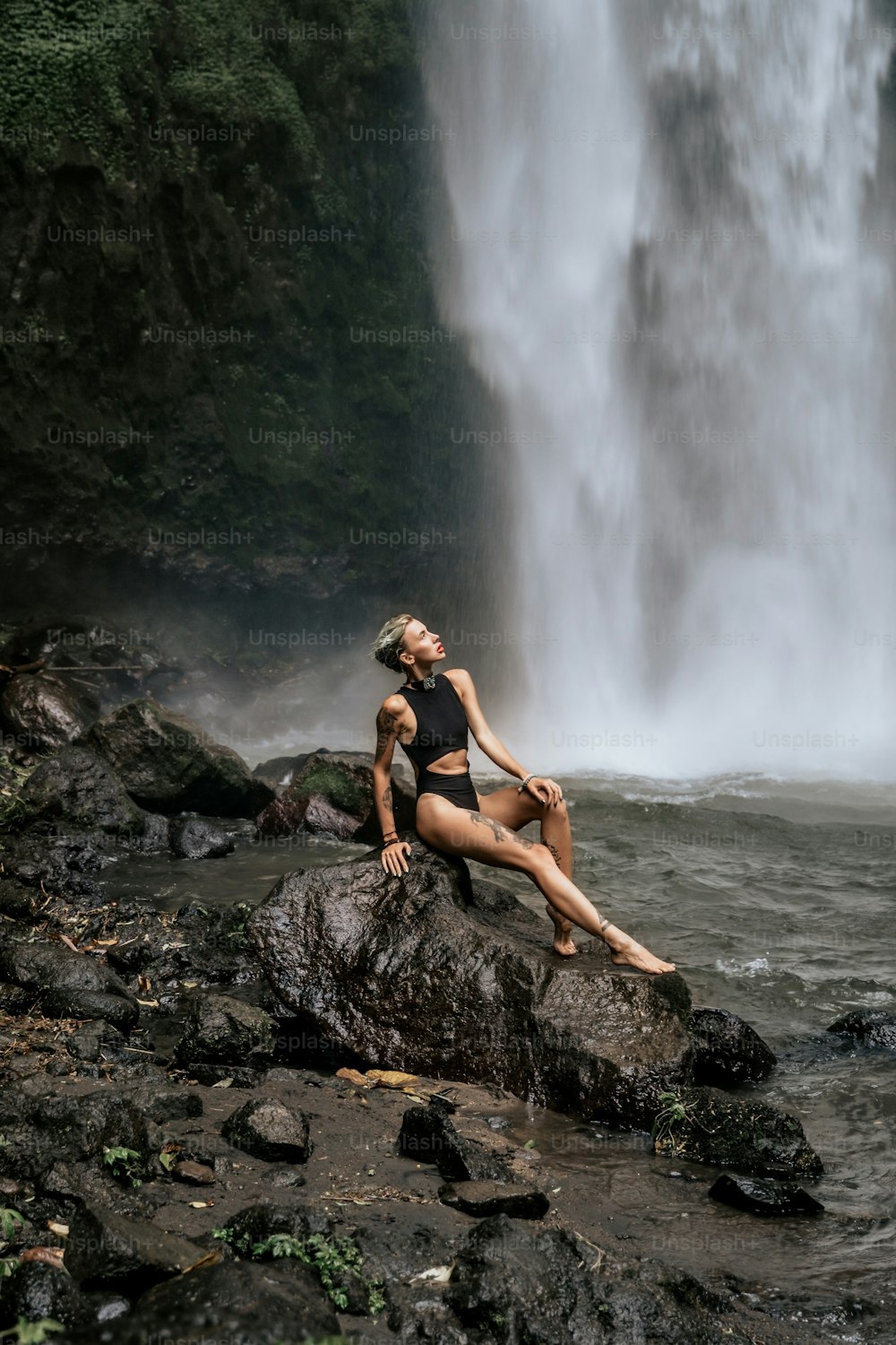 Una mujer sentada en una roca frente a una cascada