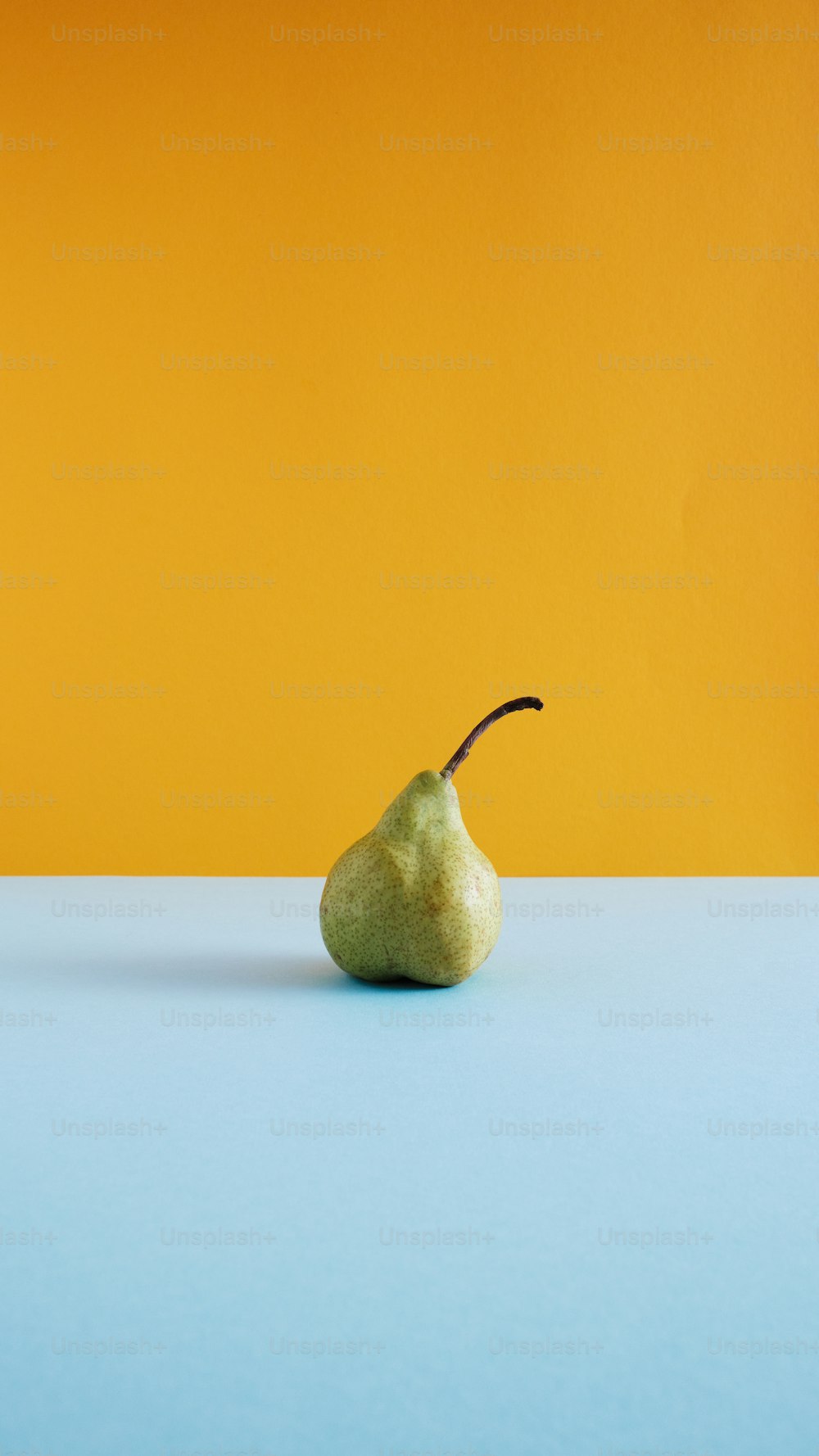 a pear on a blue surface with a yellow background