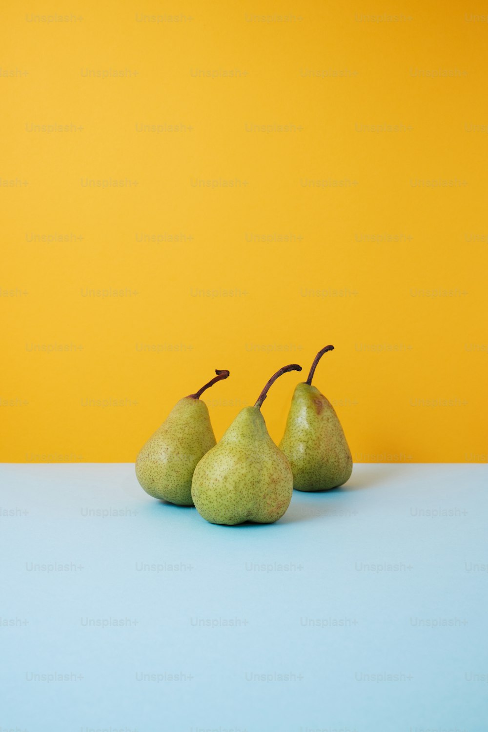 three pears sitting on a blue surface in front of a yellow wall