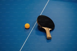 a ping pong paddle and an orange on a blue ping pong table