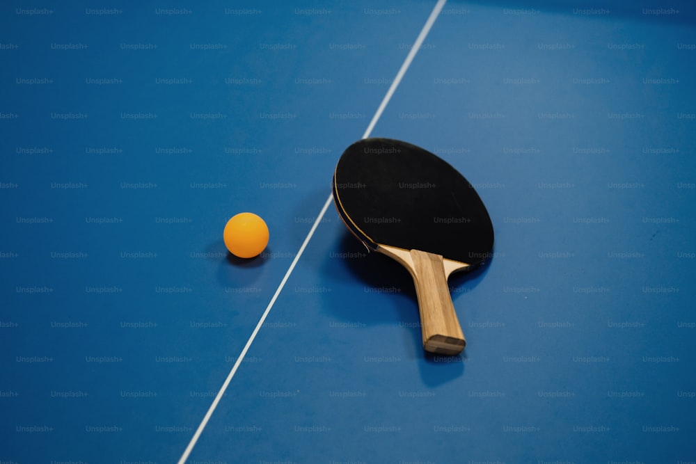 una racchetta da ping pong e un'arancia su un tavolo da ping pong blu