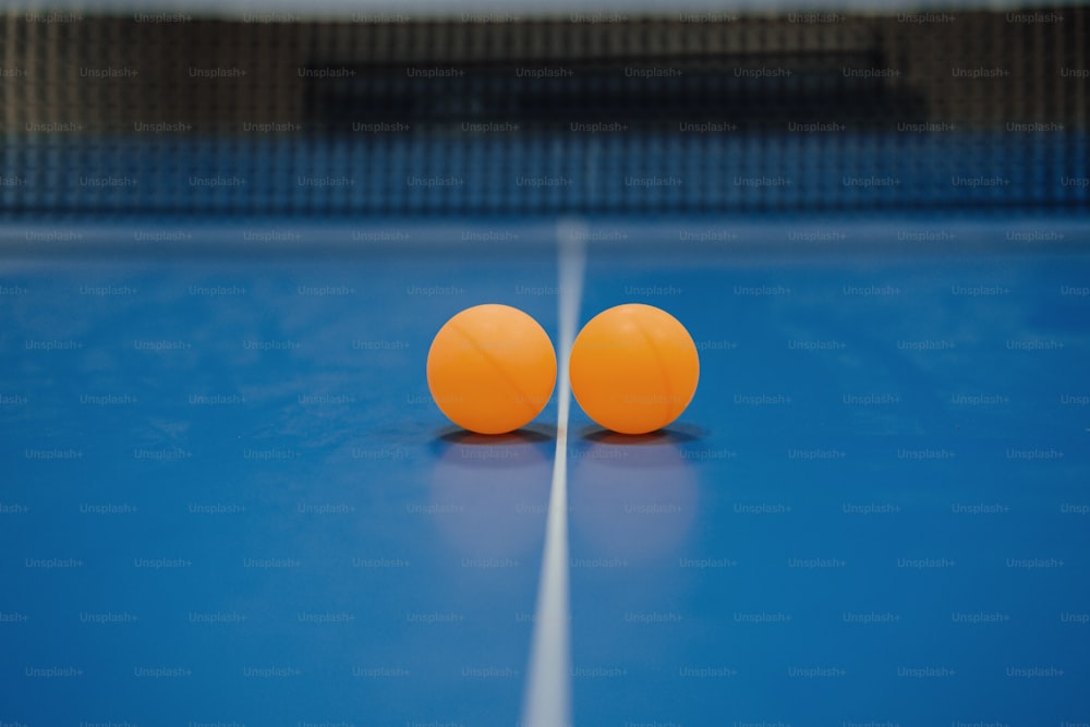 Zwei orangefarbene Tischtennisbälle auf einem blauen Tisch
