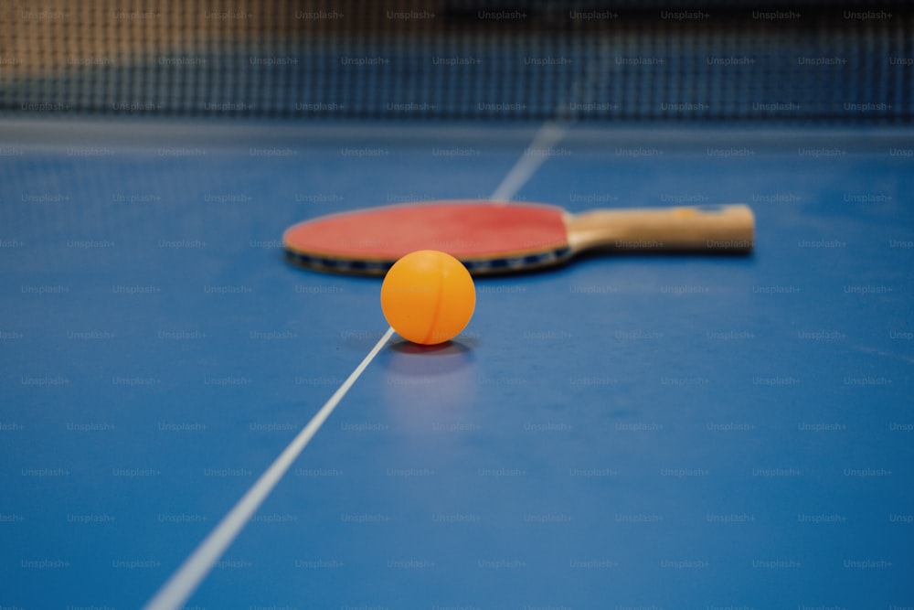 uma raquete de pingue-pongue e uma bola laranja em uma mesa azul