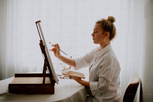 a woman sitting at a table with a easel and brush