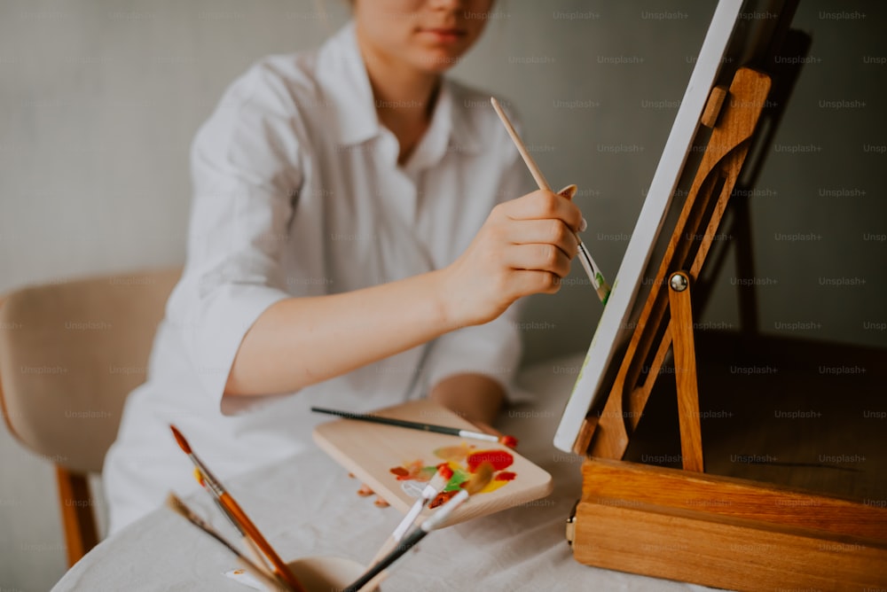 a woman sitting at a table holding a paintbrush