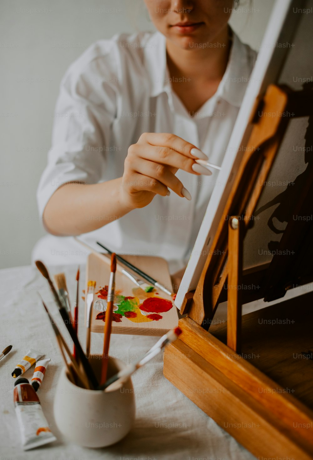 a woman sitting in front of an easel holding a paintbrush
