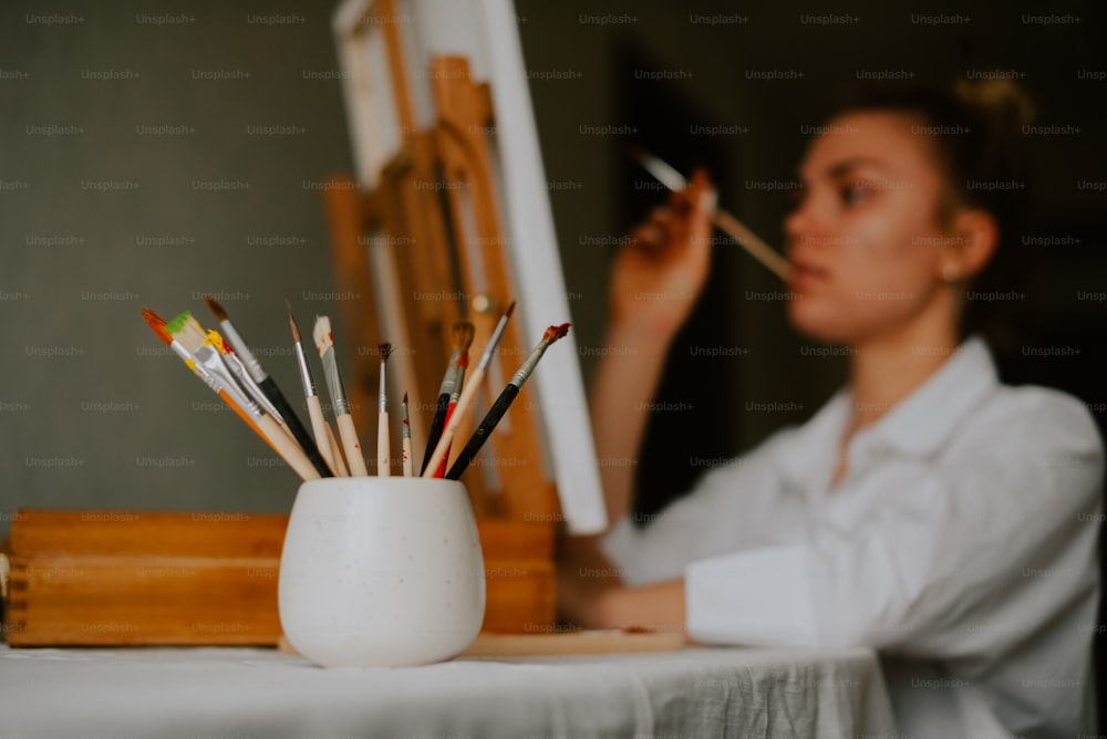 a woman sitting at a table holding a paintbrush