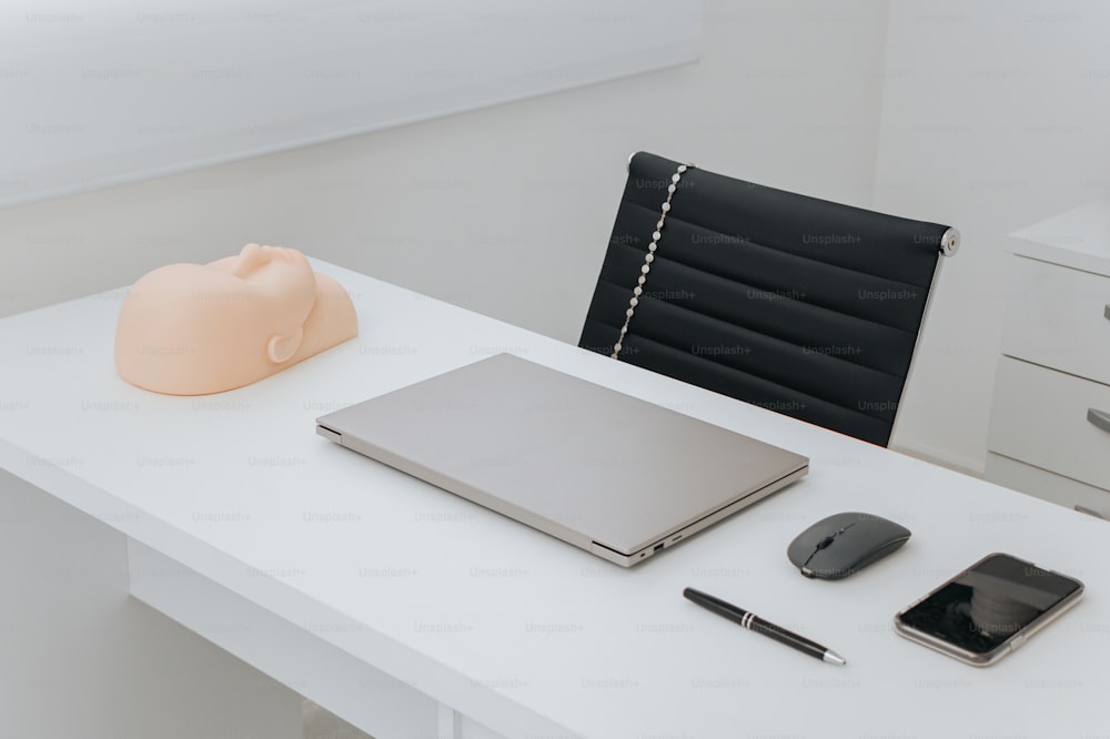 a white desk topped with a laptop computer next to a phone