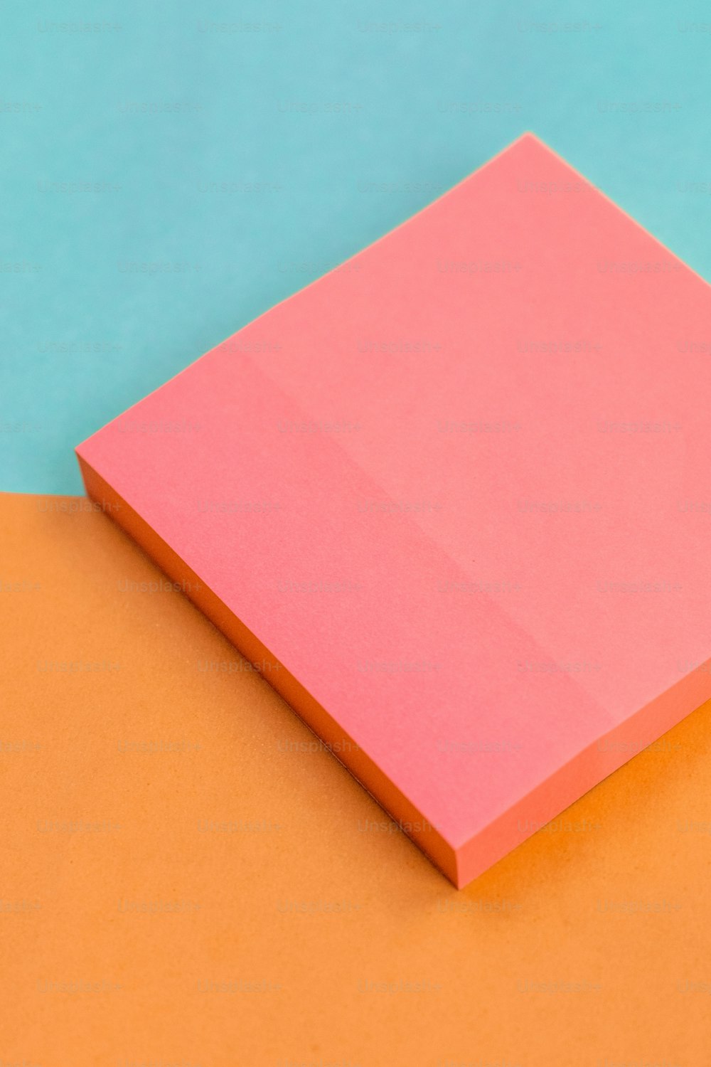 オレンジと青の表面の上に置かれたピンクの紙