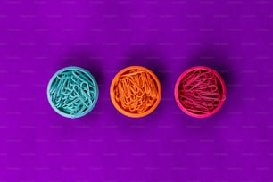 three plastic containers filled with different colored paper clips