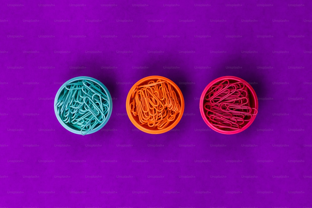 Tres recipientes de plástico llenos de clips de diferentes colores