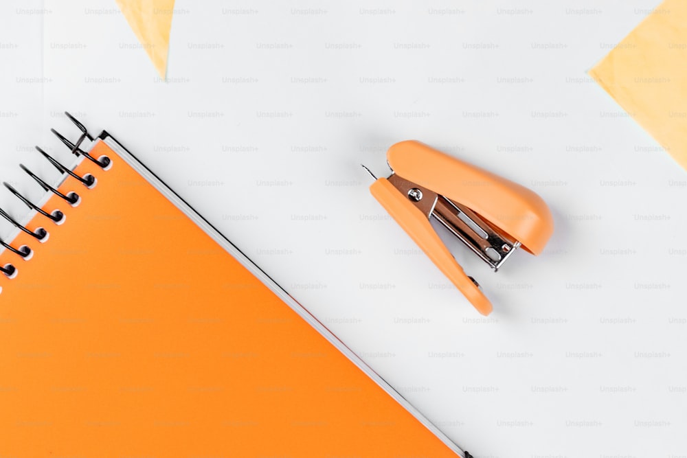 an orange notebook with a stapler and a pen