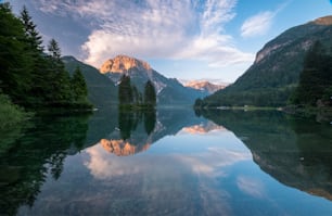 a lake surrounded by mountains and trees under a cloudy sky