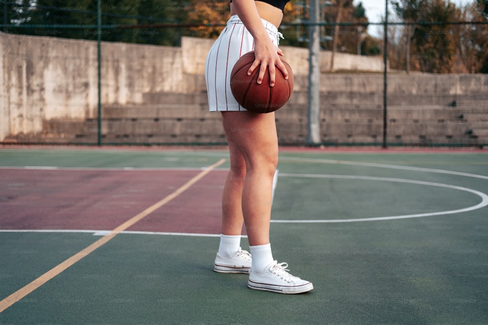 Una mujer parada en una cancha de baloncesto sosteniendo una pelota de baloncesto
