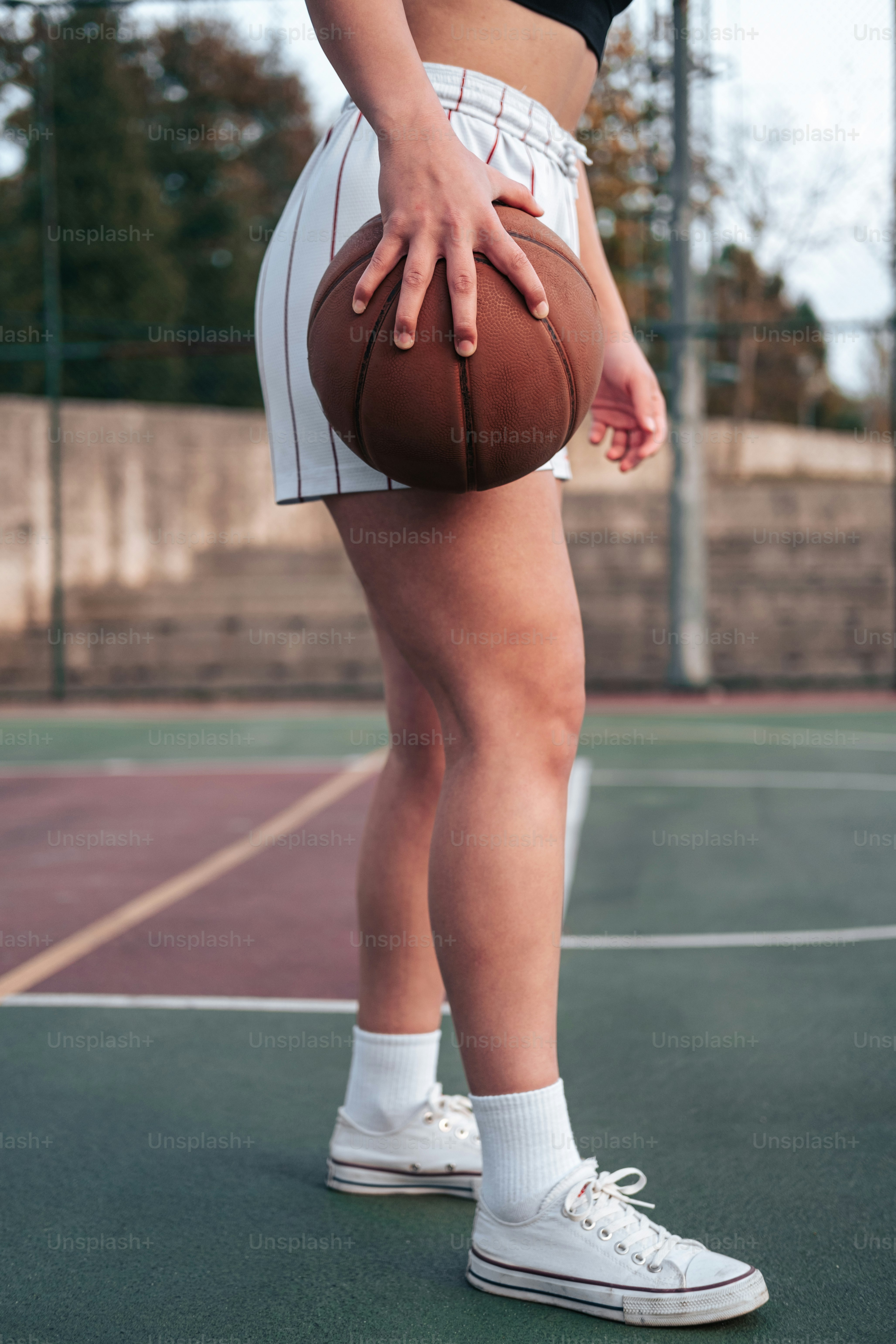 a woman holding a basketball on top of a tennis court