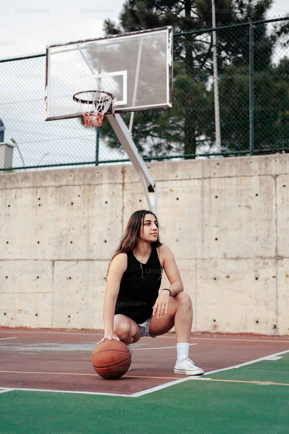 Una mujer sentada en una cancha de baloncesto sosteniendo una pelota de baloncesto