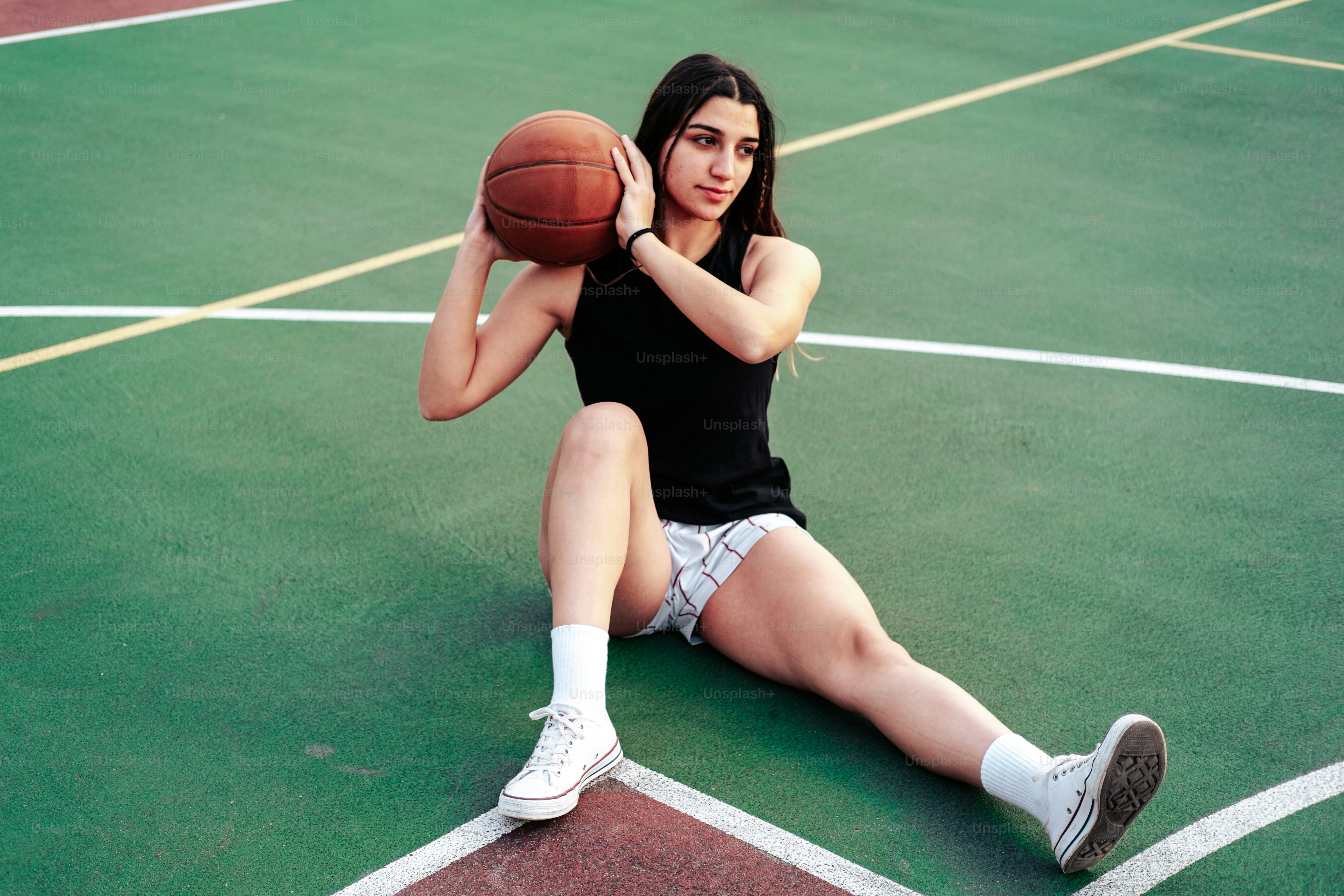 a woman sitting on a basketball court holding a basketball
