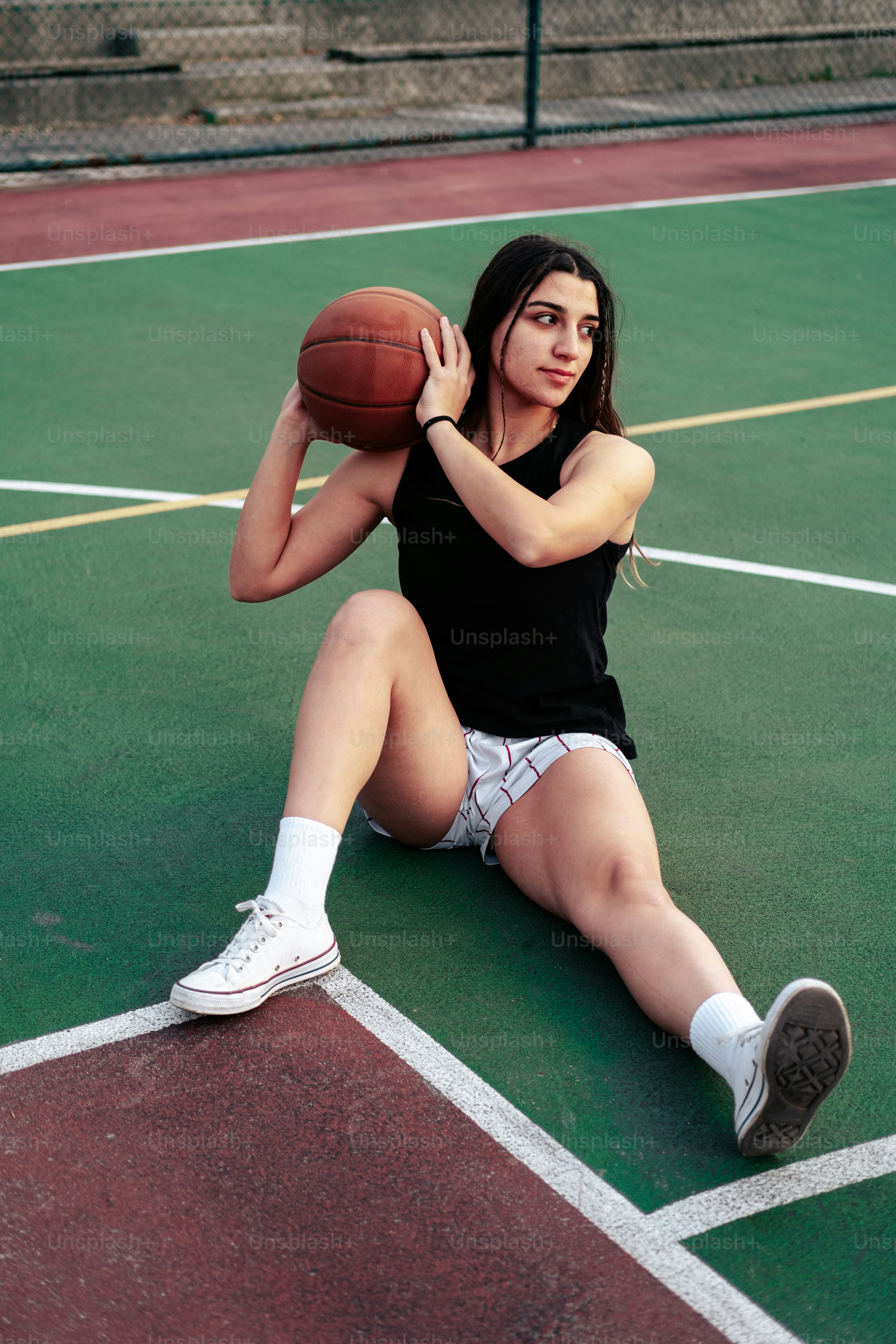 a woman sitting on a tennis court holding a basketball