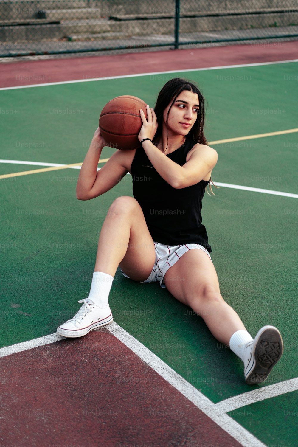 a woman sitting on a tennis court holding a basketball